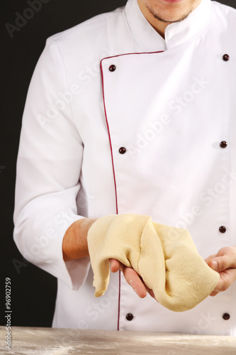 Man preparing dough basis for pizza on the wooden table, close-up