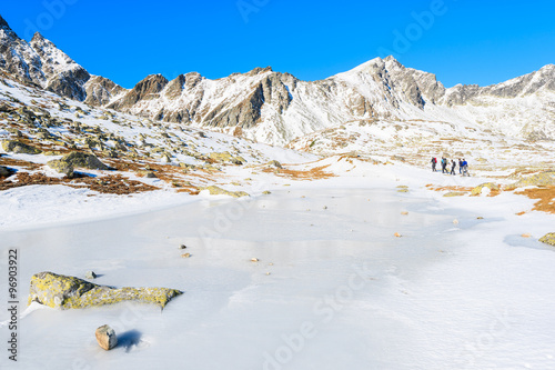 Group of tourists walking along frozen lake in Hincova valley in winter landscape of Tatra Mountains, Slovakia