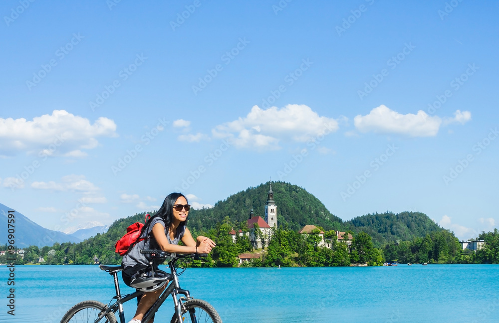 Fototapeta premium Asian tourist on a bike with beautiful scenery of lake Bled with church on island in Slovenia, Europe