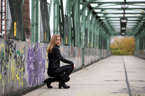Photography Beautiful blonde woman in leather jacket and leggings on a bridge