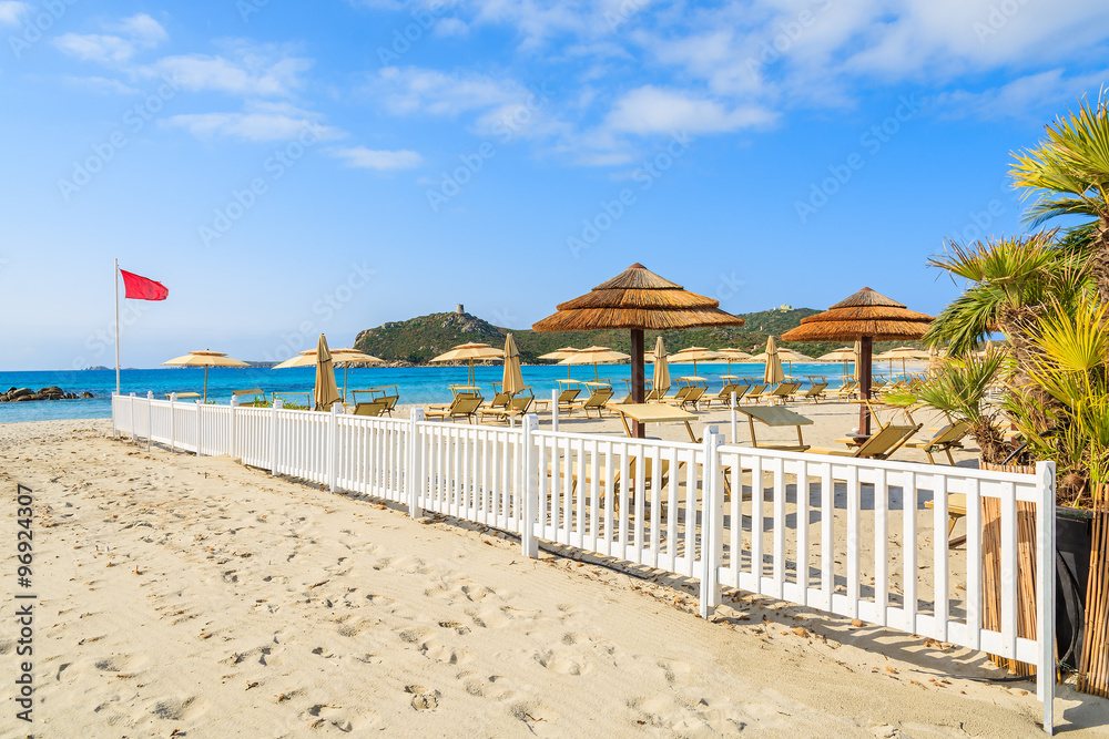 Sunchairs and umbrellas with white wooden fence at Porto Giunco beach, Sardinia island, Italy