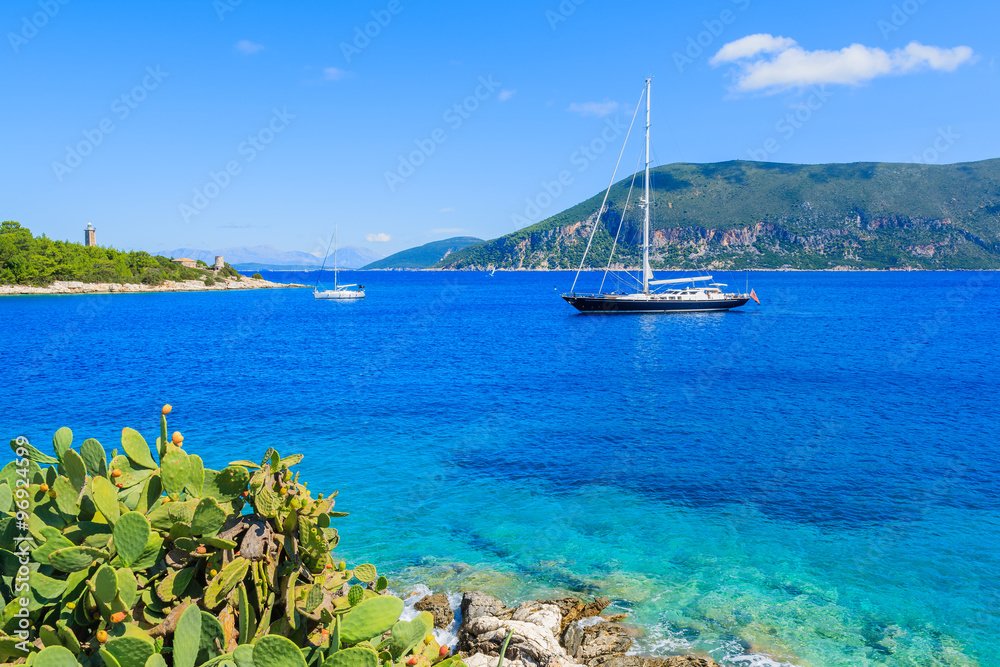 Luxury yacht boat on blue sea with green cacti plants in foreground on coast of Kefalonia island near Fiskardo village, Greece