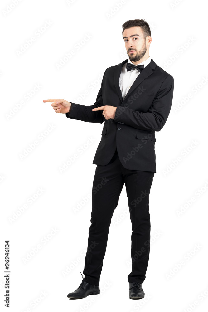 Confused luxurious man with bow tie pointing at copyspace. Full body length portrait isolated over white studio background. Confused luxurious man with bow tie pointing at copyspace. Full body length portrait isolated over white studio background.