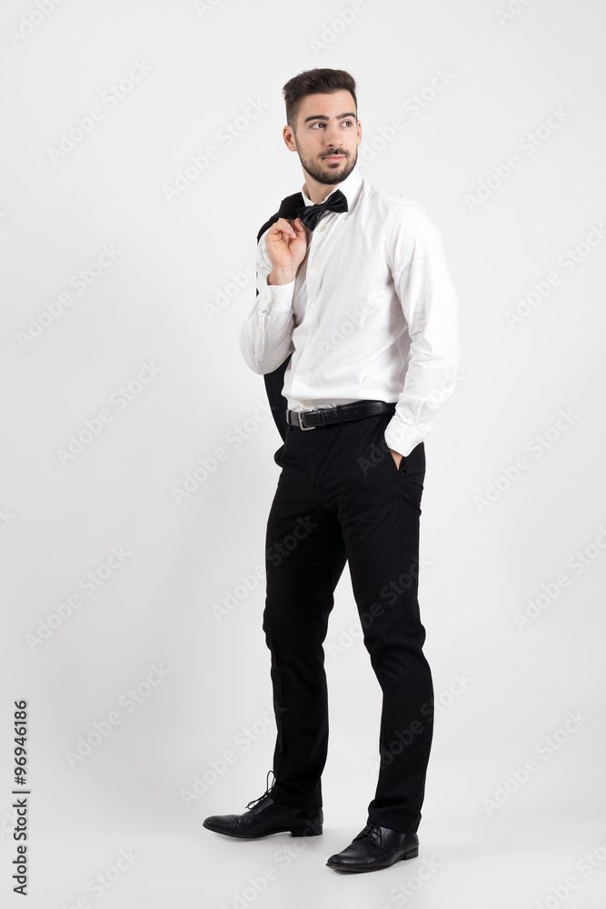 Side view of elegant man holding suit jacket over his shoulder looking away with hands in pockets. Full body length portrait over gray studio background. Side view of elegant man holding suit jacket over his shoulder looking away with hands in pockets. Full body length portrait over gray studio background.