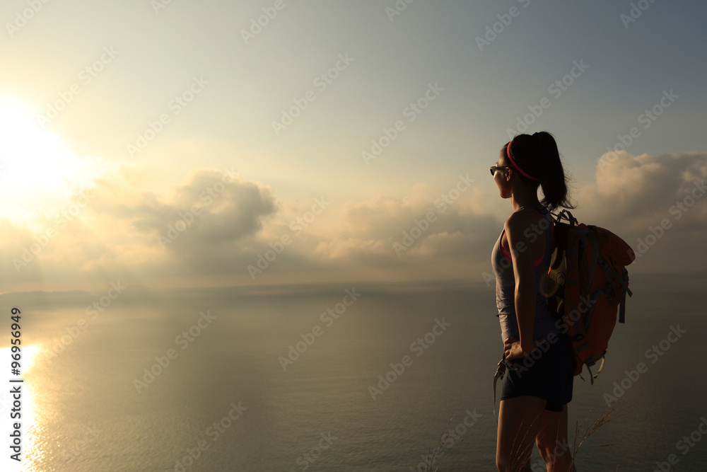 young woman backpacker at sunrise seaside mountain peak
