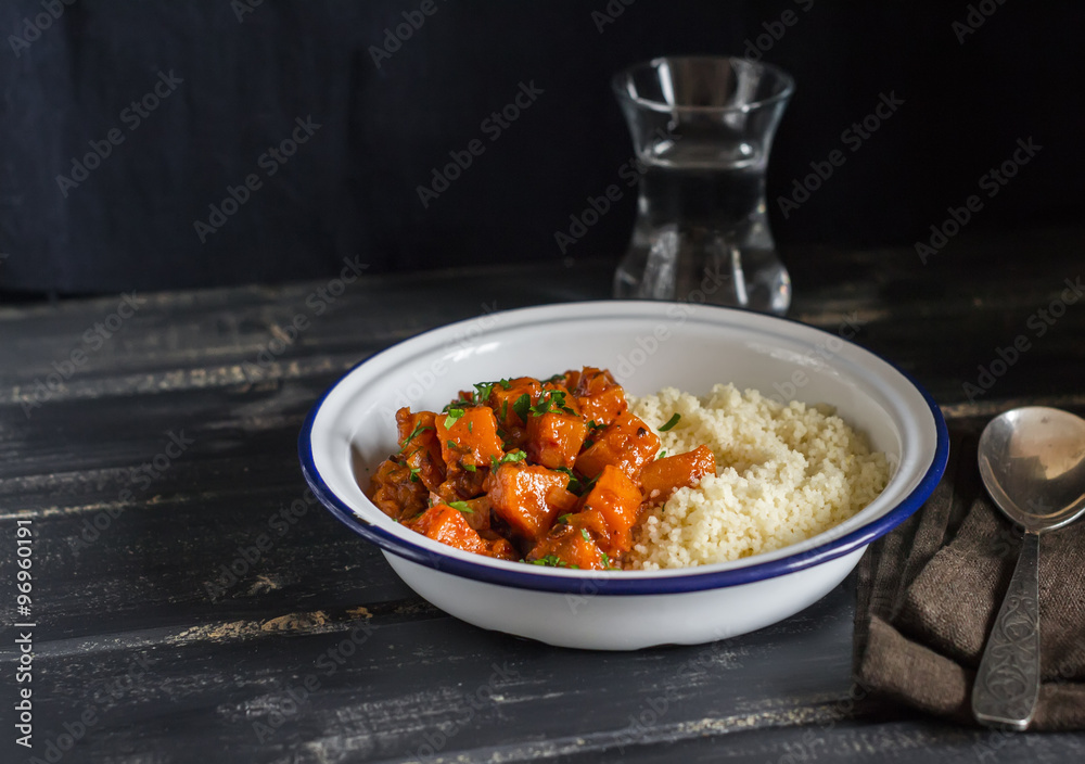 Healthy vegetarian lunch - pumpkin stew and couscous in a white enamel bowl on a dark wooden board. Rustic style Healthy vegetarian lunch - pumpkin stew and couscous in a white enamel bowl on a dark wooden board. Rustic style