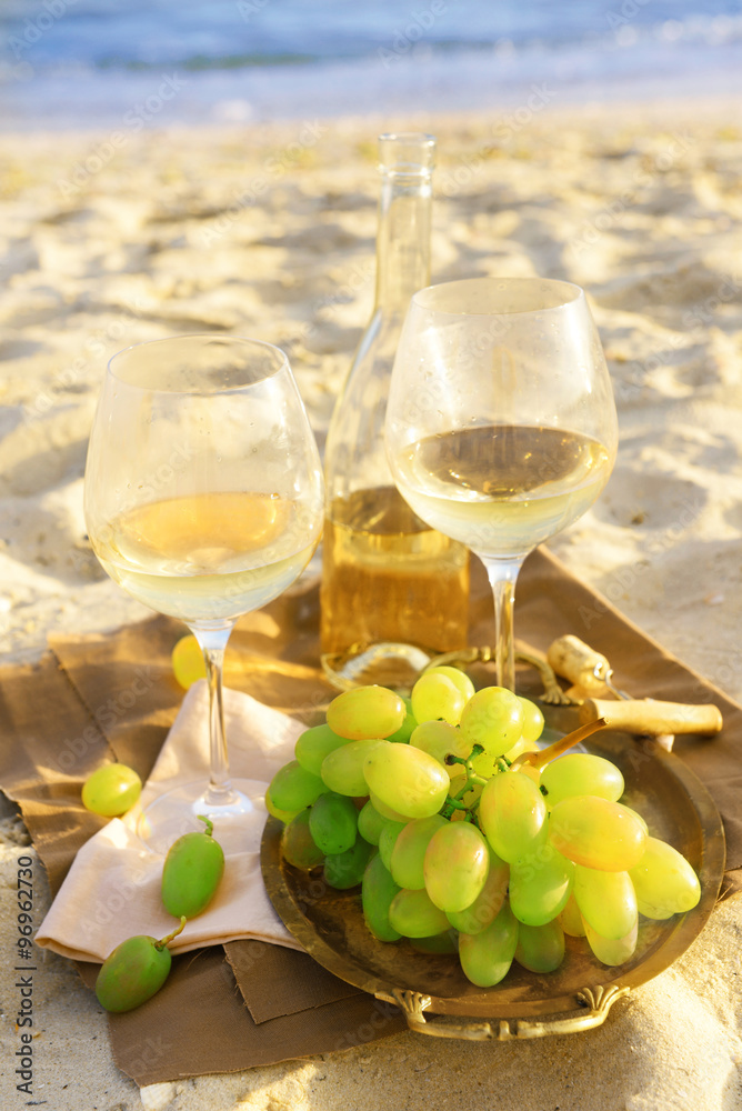 Fototapeta premium Romantic composition of white wine and grape on sandy beach