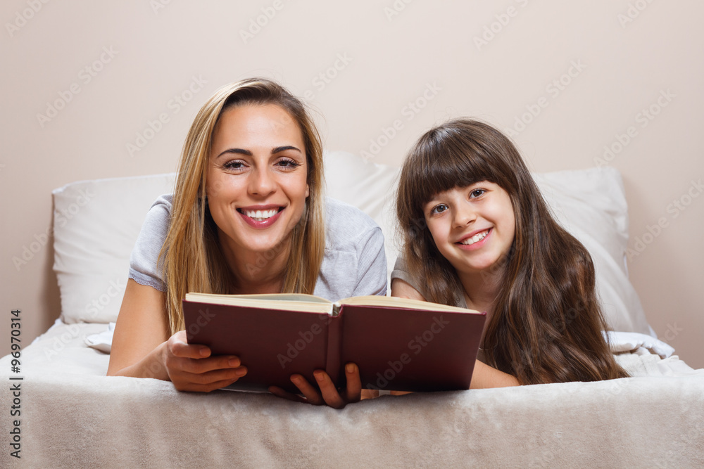 Mother and daughter reading together book in bed Mother and daughter reading together book in bed
