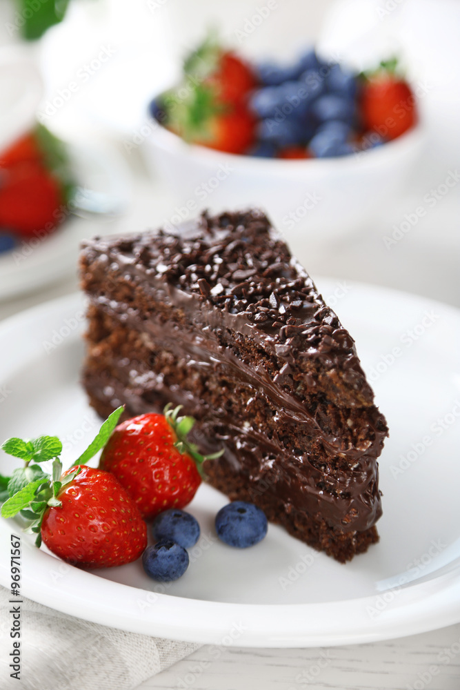 Chocolate cake with chocolate cream and fresh berries on plate, on light background Chocolate cake with chocolate cream and fresh berries on plate, on light background
