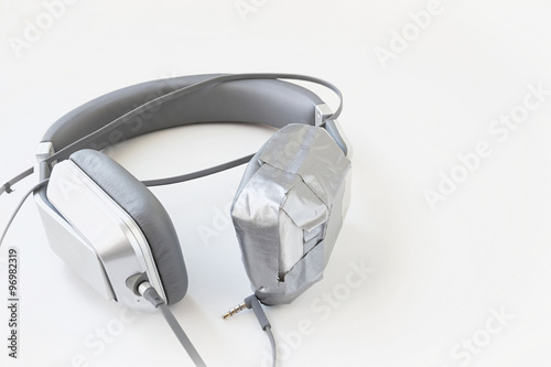 horizontal image of a pair of broken headphones that have one ear piece taped up with duct tape isolated on white background.