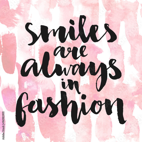 Smiles are always in fashion. Inspirational quote handwritten with black ink and brush, custom lettering for posters, t-shirts and cards. Vector calligraphy on pink watercolor strokes background