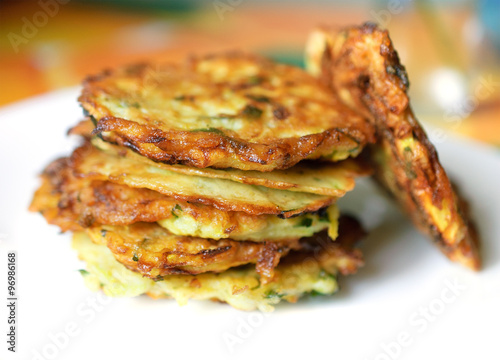 Stack of fried vegetable fritter made of zucchini, eggs, parsley, decorated with a sprig of green onions on a white plate. Selective Focus, Focus on the front of the top fritters