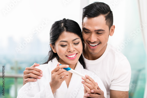 Asian couple with pregnancy test in bed