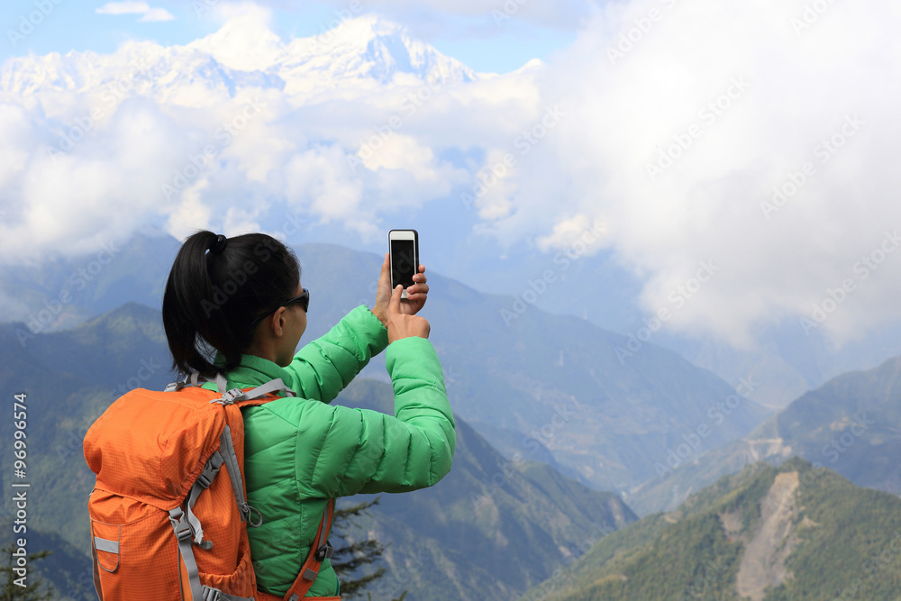 young asian woman backpacker taking photo with smartphone on mountain peak