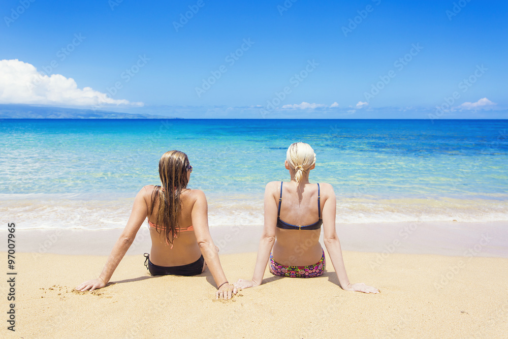 Two women sun tanning on a sunny beautiful beach. View from behind of women relaxing while on a beautiful island vacation
