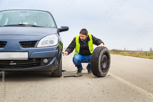 Man replacing a tire on his car by the road © cherryandbees