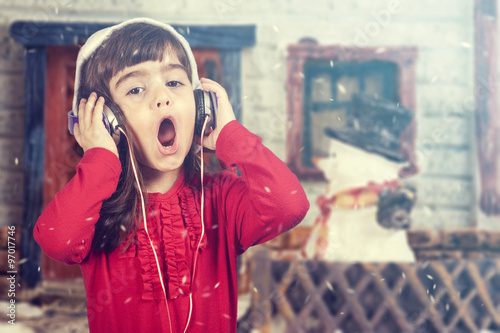 Adorable little girl wearing a Santa hat listening to music and singing Christmas carols. Cross processed image with shallow depth of field photo