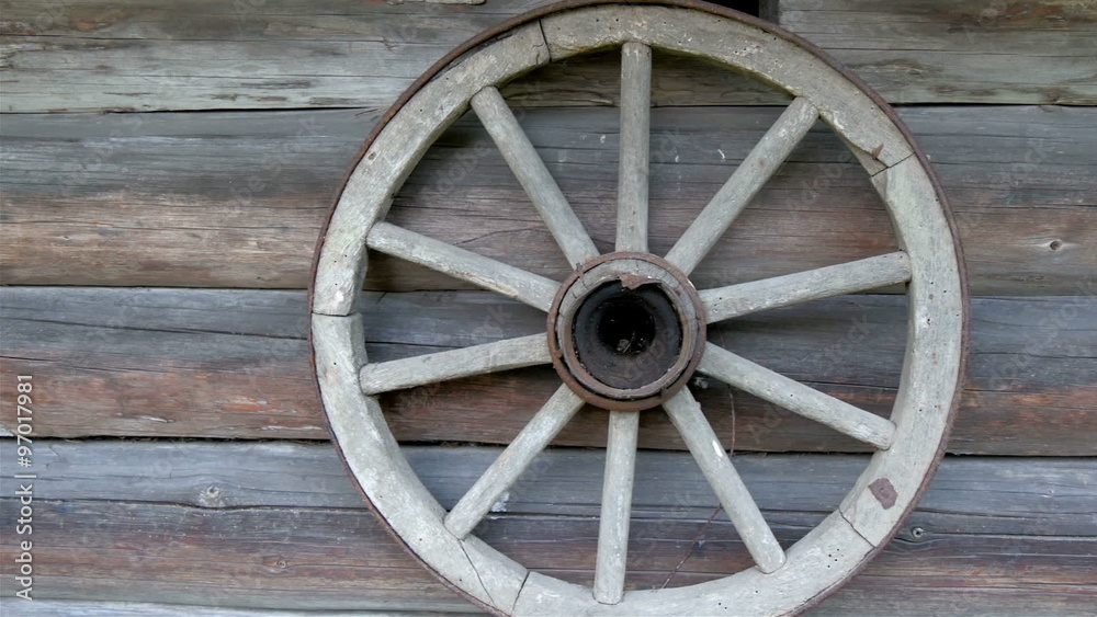 The round wheel hanging on the wall of the house. It serves as the decoration outside the log house The round wheel hanging on the wall of the house. It serves as the decoration outside the log house