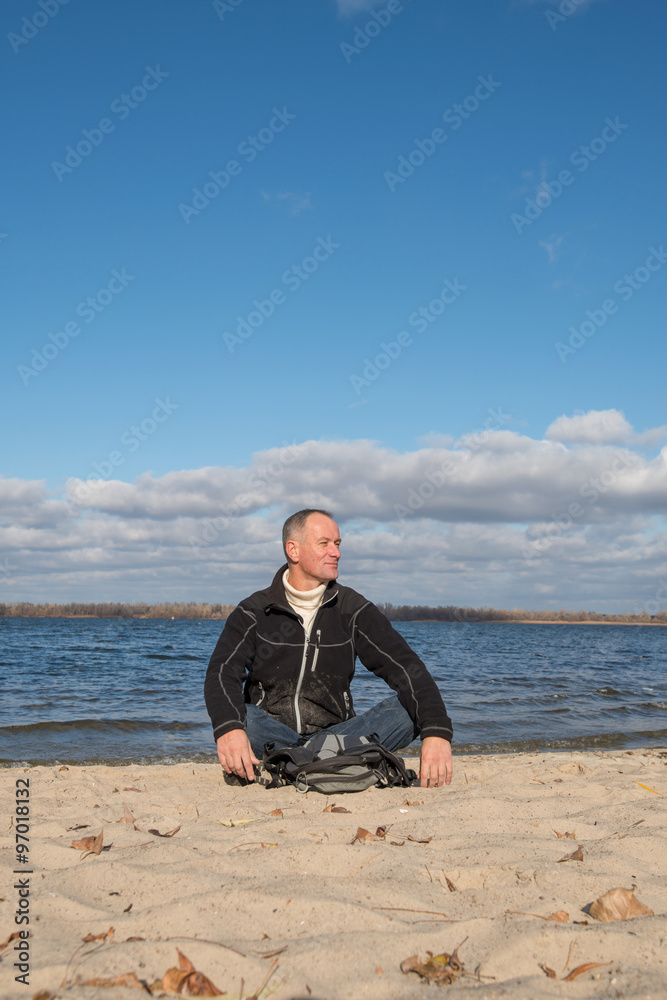 Hiker man sitting on the beach, smiling, relaxing and enjoying l