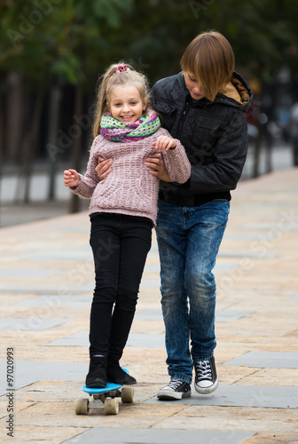  girl learning to ride skateboard, teenage brother supporting he