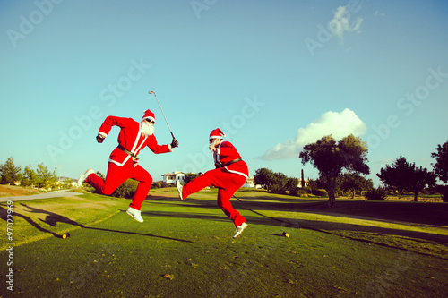 Two Santa Claus jumping on a golf course