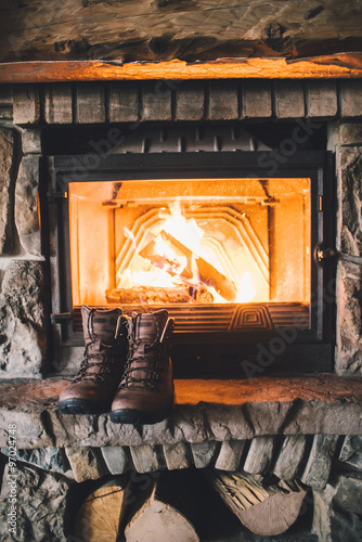 Winter boots in front of a fireplace. Pair of vintage folk boots drying near the fireside. Warm cozy fireplace in the authentic chalet. Hipster shoes getting warm near the burning fire in a cabin
