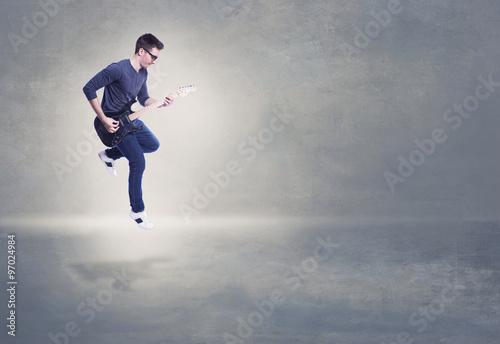 Addicted to music. Young man playing electric guitar jumping on background