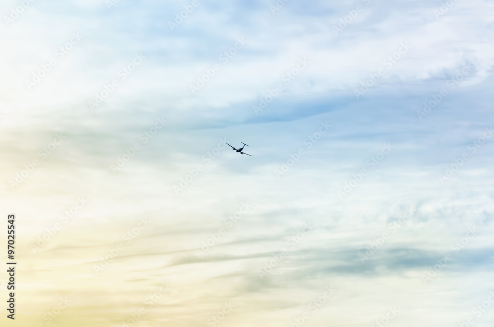 Silhouette of small plane, at horizon. It's flying when the dawn is about to break, at a cloudy day. Beautiful yellow and blue colors contrast.