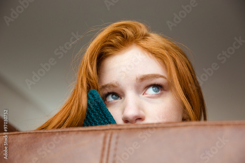 Fotografie Unconfident shy redhead girl peeping from sofa