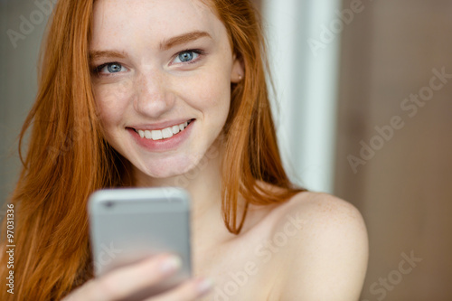 Smiling redhead woman holding smartphone
