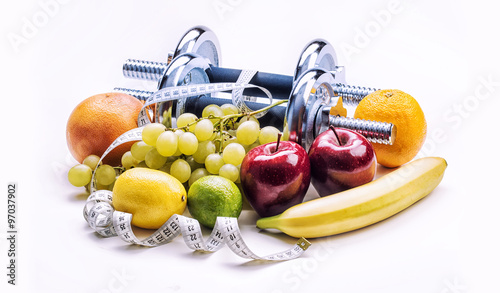 Chrome dumbbells surrounded with healthy fruits measuring tape on a  white background with shadows. Healthy lifestyle diet and exercise. photo