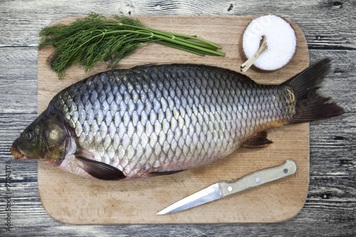 A large fresh carp live fish lying on a wooden board with salt and dill.