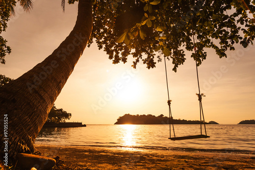 Tropical sea beach with swing tied at sunset photo