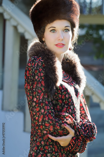 Cheerful Russian beauty in traditional fur Cossack hat and crossed hands