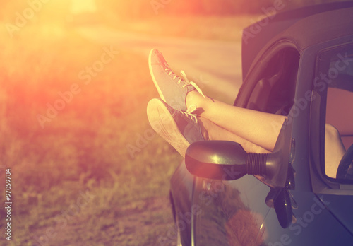 Vintage photo of woman's legs in retro shoes out of car windows in summer sunset