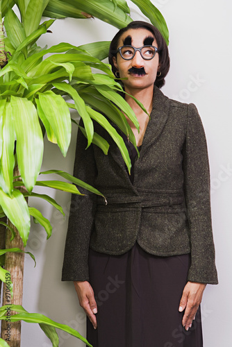 Businesswoman hiding behind plant wearing disguise photo