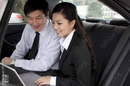 Businesspeople working on laptop in back of car © xixinxing