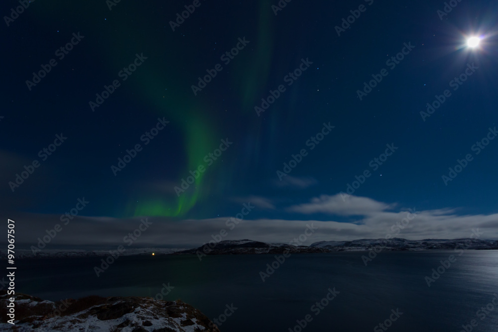 Aurora in the sky in a full moon night on the shores of the Barents Sea
