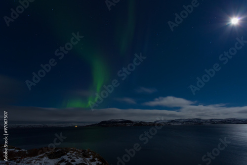 Aurora in the sky in a full moon night on the shores of the Barents Sea