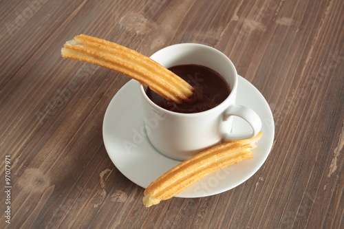 cup of liquid chocolate and churros on a wooden table