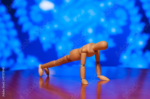 Wooden dummy, mannequin or man figurine exercising - doing a plank, press-up, push-up on blue background