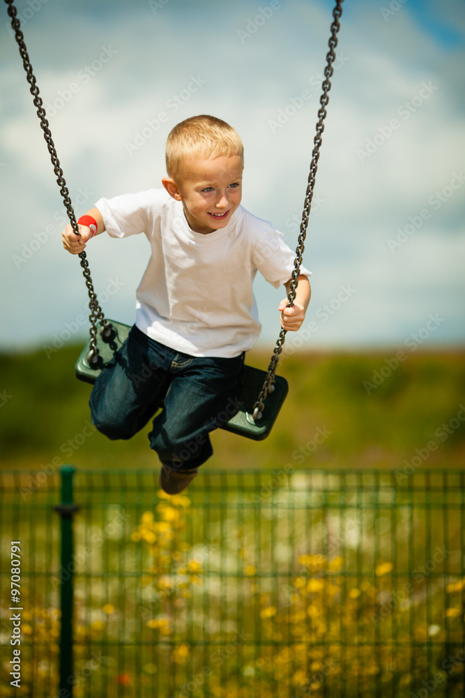 Little blonde boy child having fun on a swing outdoor