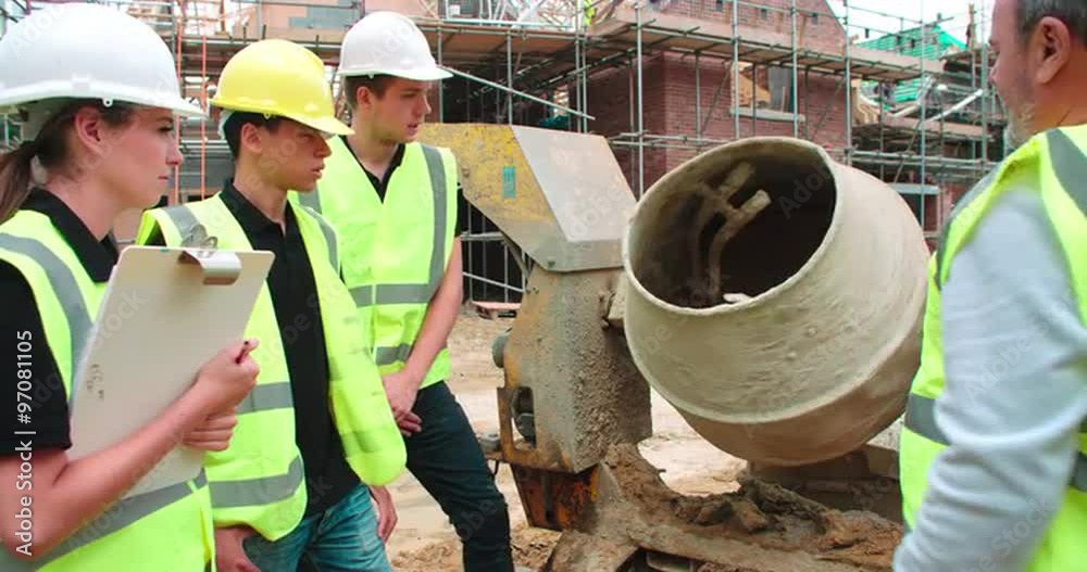 Builder Using Cement Mixer On Building Site With Apprentices