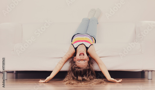 Foto Little girl kid with long hair upside down on sofa