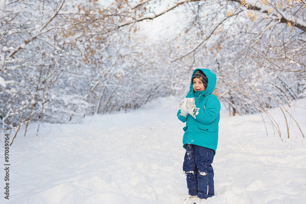 A cute little boy stands and keep snow in park