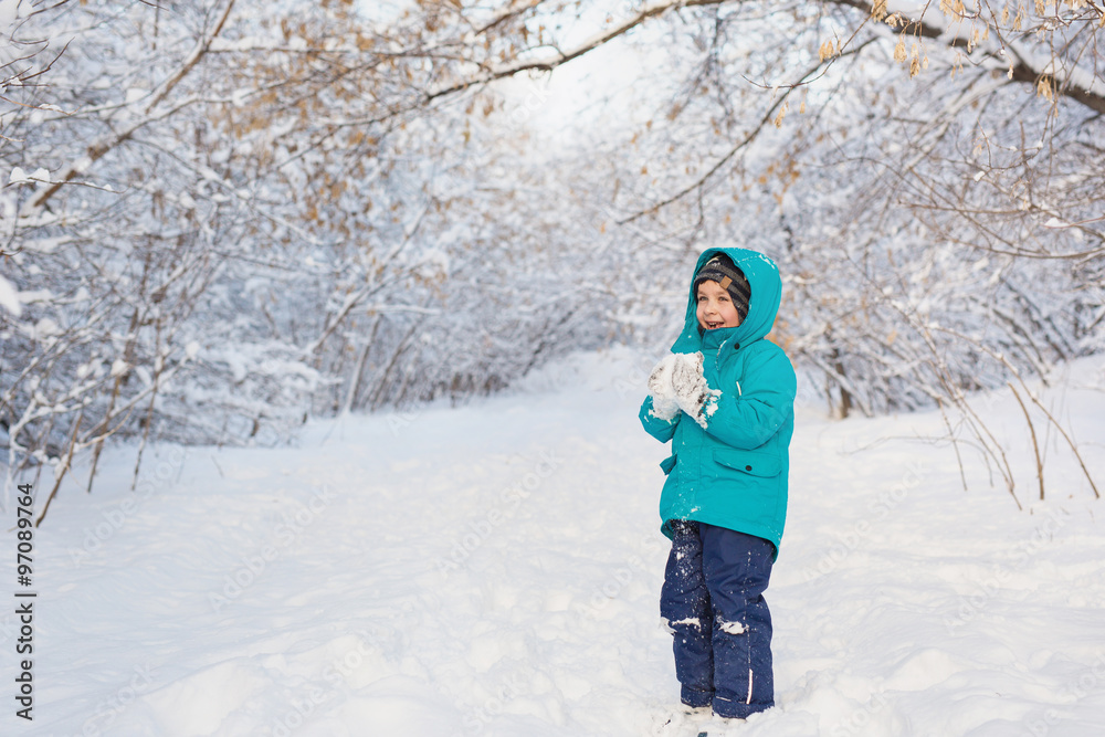 A cute little boy stands and keep snow in park A cute little boy stands and keep snow in park
