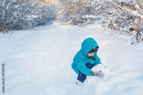 A cute little boy plays with snow in winter forest