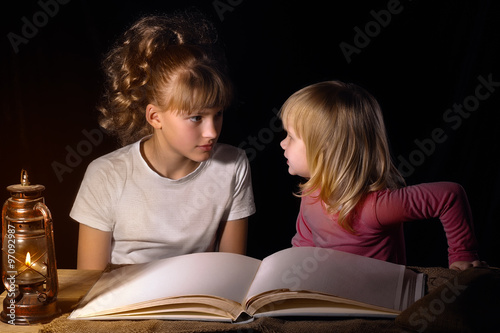 Две сестры рассказывают друг другу страшные истории на ночь. Открытая книга, старинная лампа (керосиновая). Черный фон. Семья. Детям интересно и страшно. Сказка на ночь