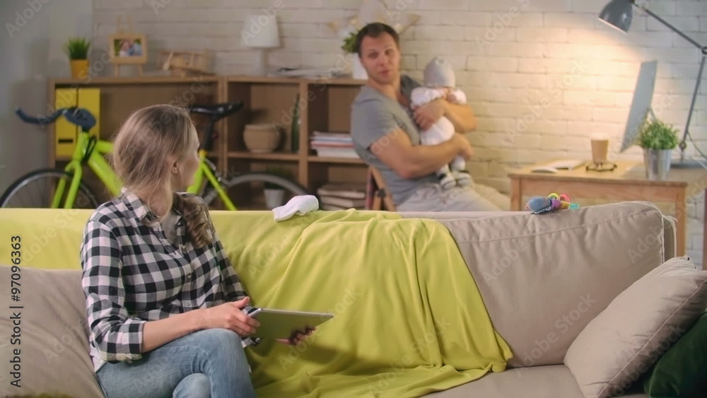 Beautiful young mother using tablet computer and talking to father rocking their baby son Beautiful young mother using tablet computer and talking to father rocking their baby son