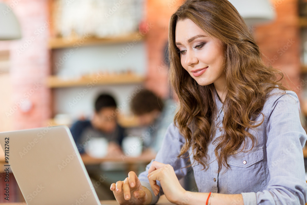 Beautiful young woman sitting in cafe and using laptop Beautiful young woman sitting in cafe and using laptop
